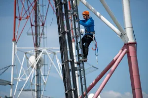 Technicien télécom escaladant un pylône pour moderniser un réseau mobile 4G avec des fonctionnalités avancées, visant à augmenter les débits