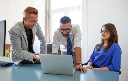 Deux hommes et une femme collaborant autour d’un ordinateur portable lors d’une réunion, illustrant la mise en place d’une solution de portabilité des numéros fixes.