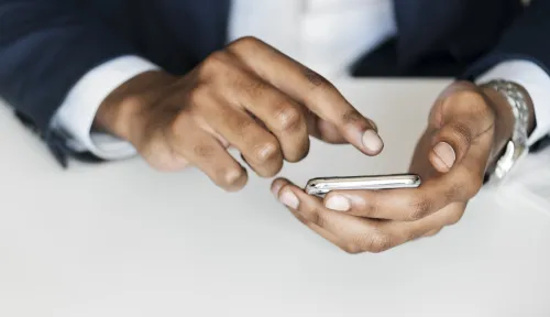 Main d’un homme utilisant un smartphone, symbole de la digitalisation croissante des services publics.

