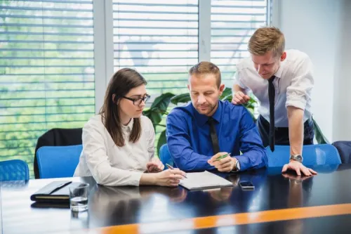 Three professionals in a meeting discussing a telecom and digital business training program.